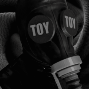 A rubber man wearing gasmaks with a gasmask with custom eye covers, with "TOY" written on it
