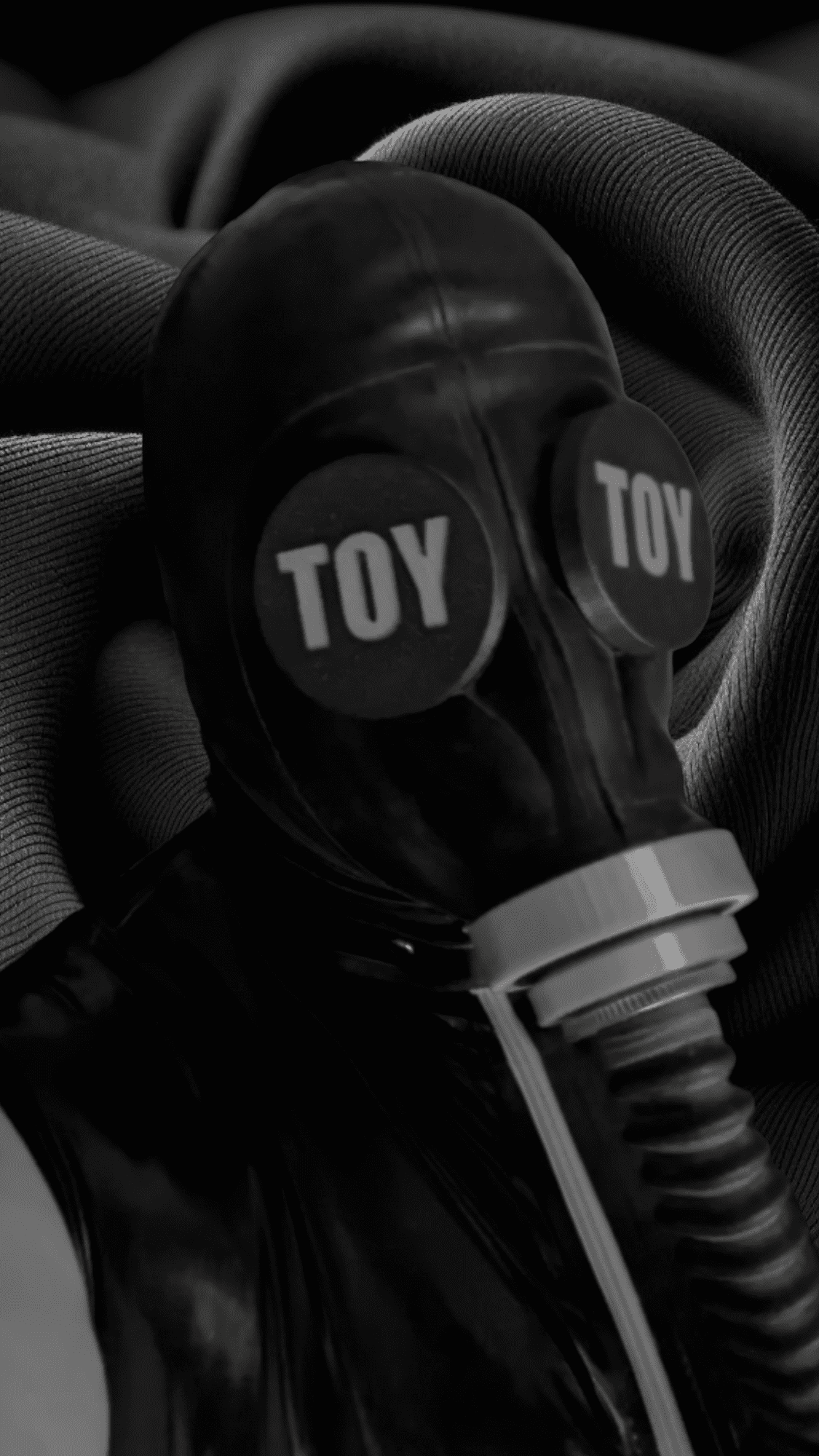 A rubber man wearing gasmaks with a gasmask with custom eye covers, with "TOY" written on it