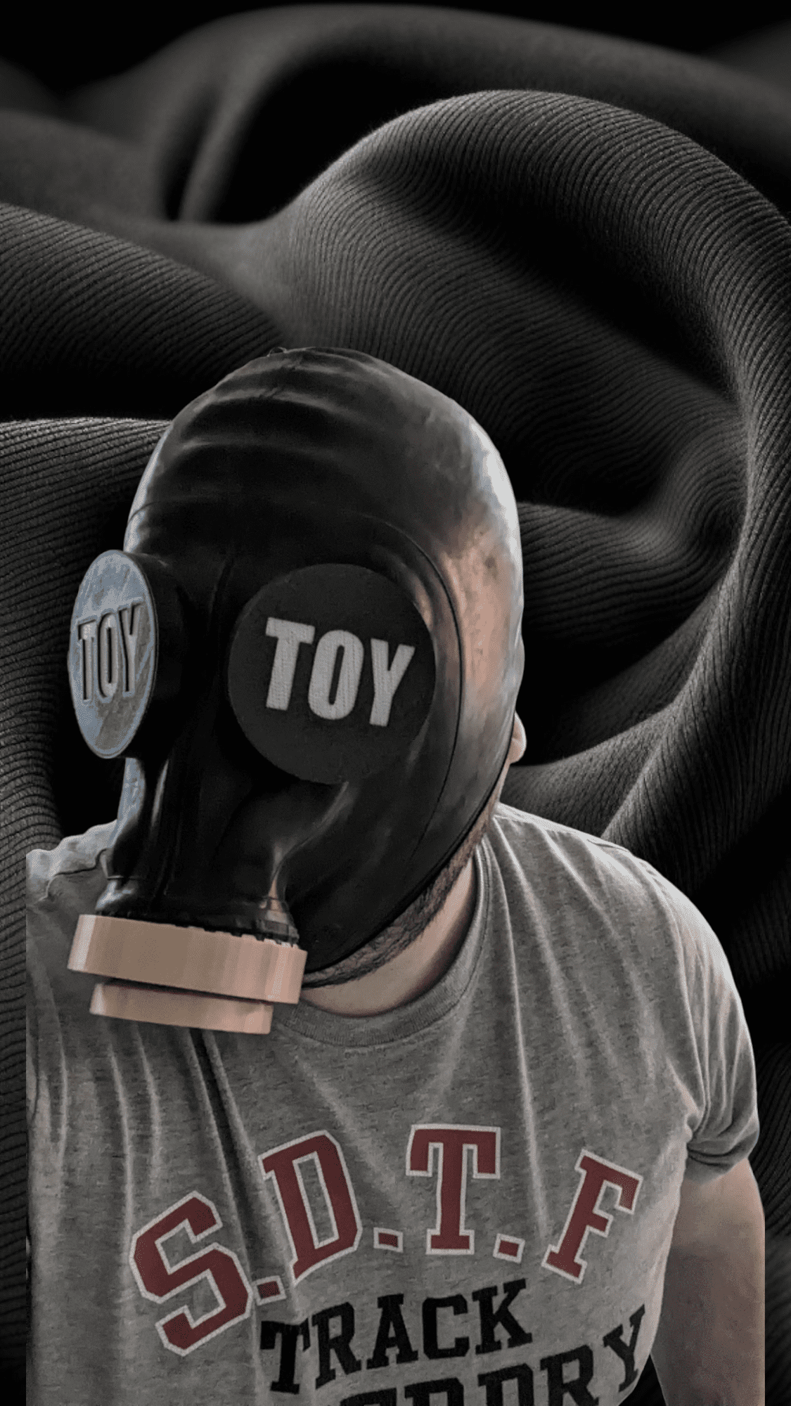 A man wearing gasmaks with a gasmask with custom eye covers, with "TOY" written on it